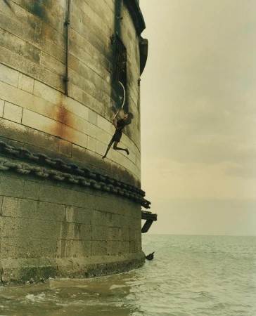 Figure rappelling down the exterior stone wall of a coastal fortress above choppy water