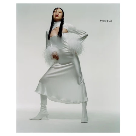 Model wearing a white cut-out dress with feathered cuffs and white boots against a neutral studio backdrop.