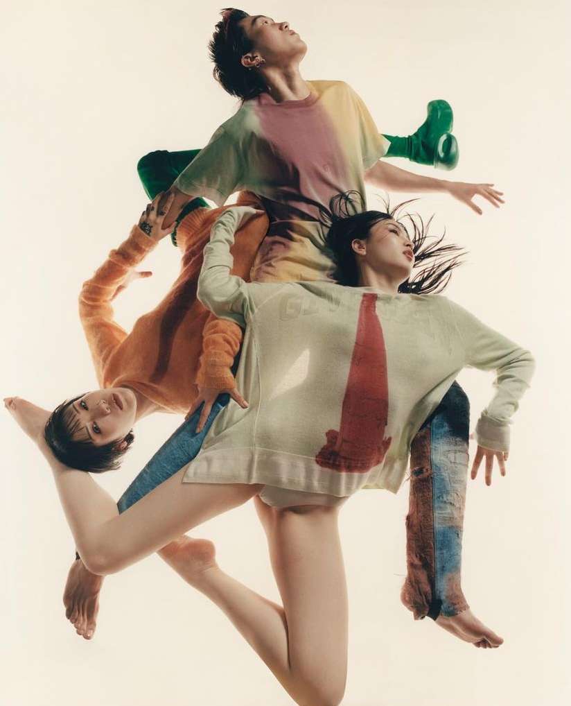 Three fashion models pose stacked on top of each other in a studio wearing colorful casual streetwear against a plain white background.