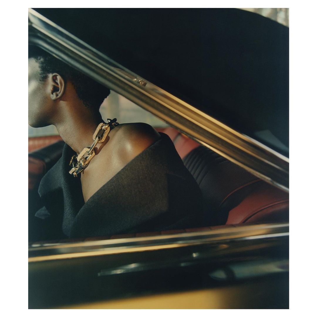 Fashion shot in car interior: Woman wearing statement chain necklace and black blazer with red leather car seat background.