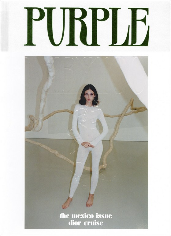 Magazine cover featuring a model in a white bodysuit posing in front of an art installation, with 'PURPLE' in green text above.