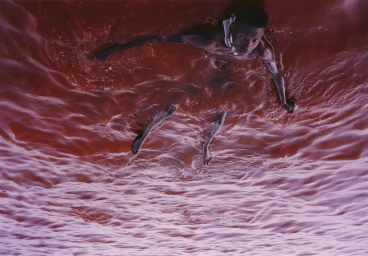 A young Black man swimming in turbulent deep red water captured from an overhead angle by Markn.