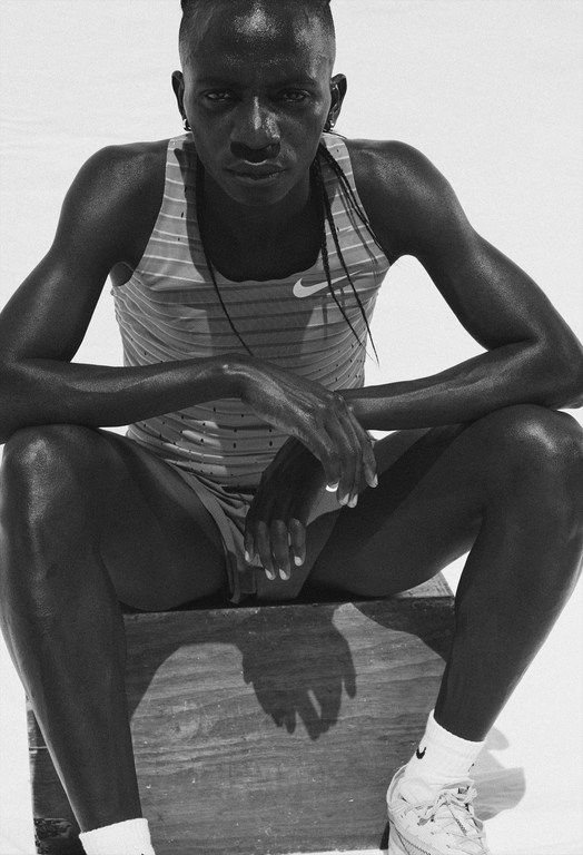 Monochrome portrait of a male athlete in sports attire seated on a wooden crate, capturing a contemplative mood in bright, diffused lighting.
