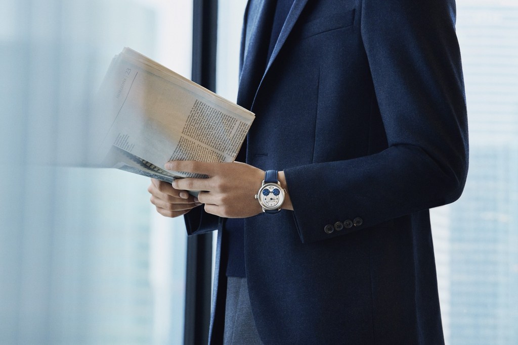 Man in a navy suit reads a newspaper near a window with a watch on his wrist. The watch has a cartoon-character design.