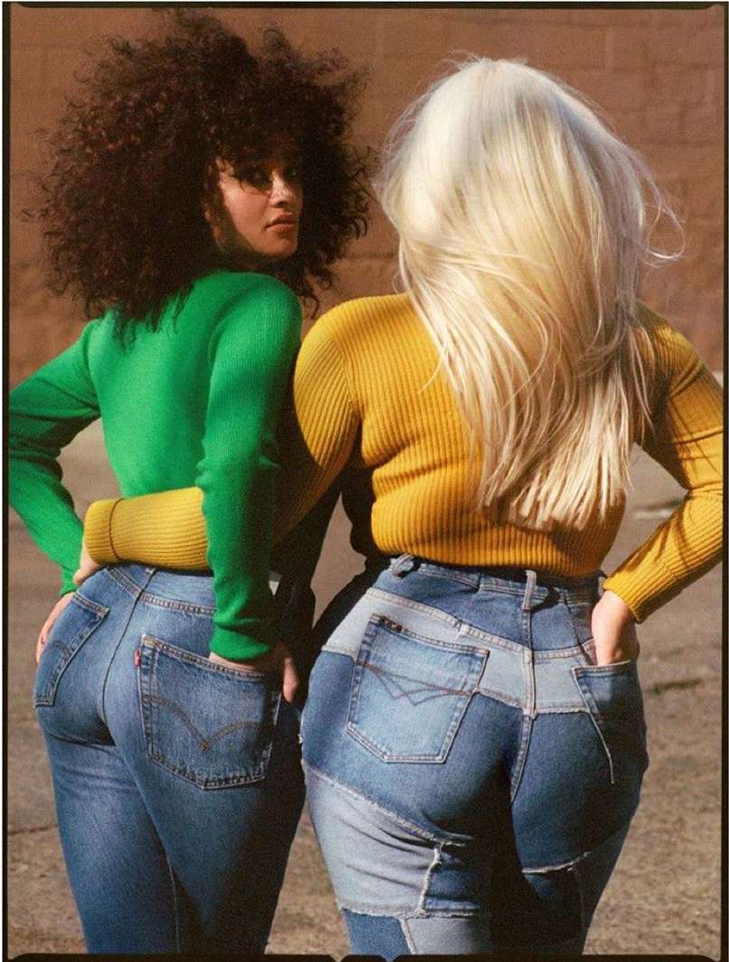 Two women with contrasting hair colors pose in cropped view wearing sweaters and jeans, showcasing fashion and casual style outdoors.