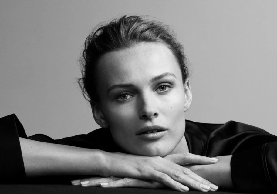 Monochrome portrait of a fair-skinned adult woman with a neutral expression, wearing a dark, satin top, resting her face on her hands.