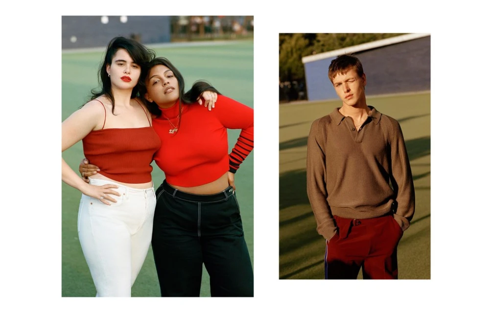 Two women pose in red tops and contrasting pants outdoors, with a male model in a brown shirt and red pants on the right.