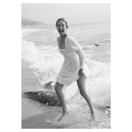 Woman in white dress laughing while running through ocean waves on a sandy beach
