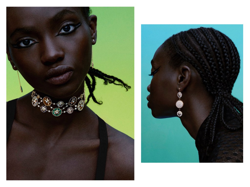 Close-up of a Black woman wearing jewelry: a layered choker necklace and hanging earrings, against a graduated green and blue background.