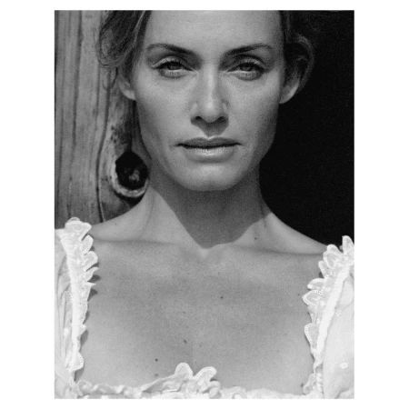 Close-up black and white portrait of a woman in a ruffled white top against a textured wooden background.