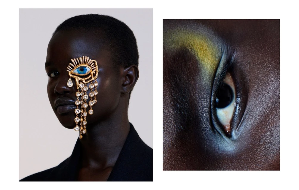 Headshot of a woman wearing a large gold eye pendant earring with crystal fringe and makeup in a white studio setting.