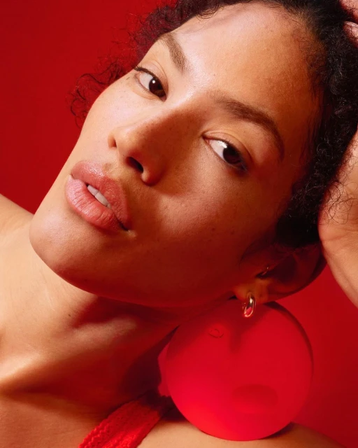 Close-up portrait of a woman with tan skin and large, red, round earrings against a matching red background in eye-level, portrait framing.