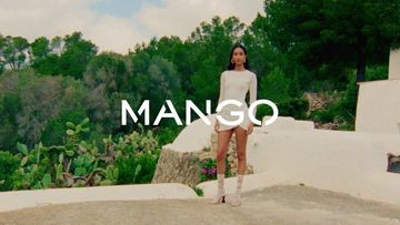 A woman in a white dress stands on a patio against a lush green landscape, promoting Mango fashion with a bright, sunny ambiance.