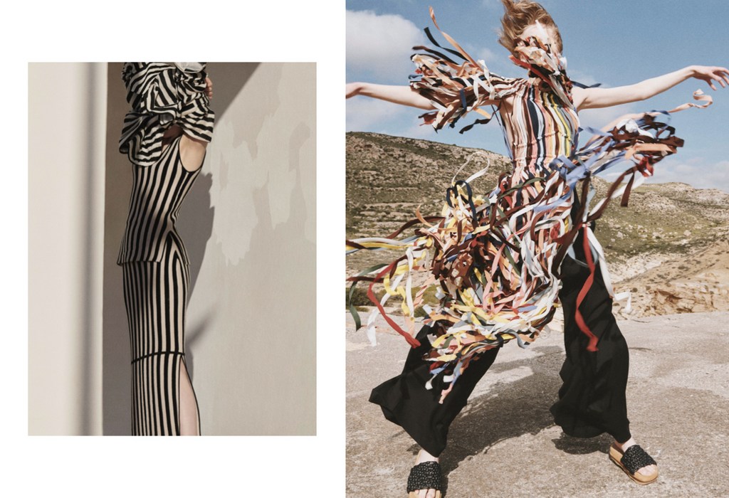 Two fashion models pose in striped dresses against a desert backdrop. The model on the right is styled with colorful ribbons.