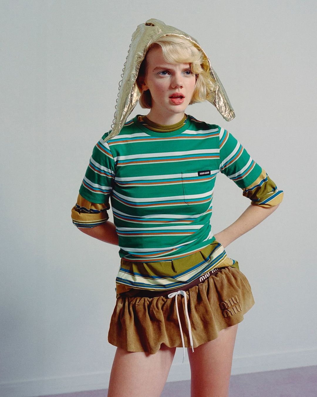 Stylish woman in striped shirt and gold headwear posing in a studio setting. Fashion-forward look with youthful expression and contemporary style.