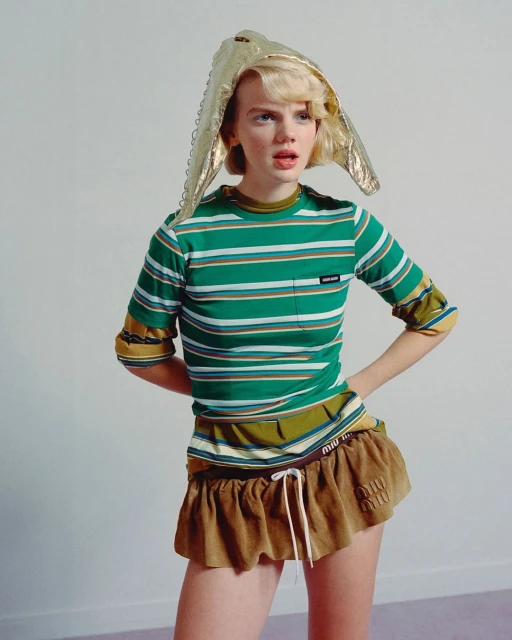 Stylish woman in striped shirt and gold headwear posing in a studio setting. Fashion-forward look with youthful expression and contemporary style.