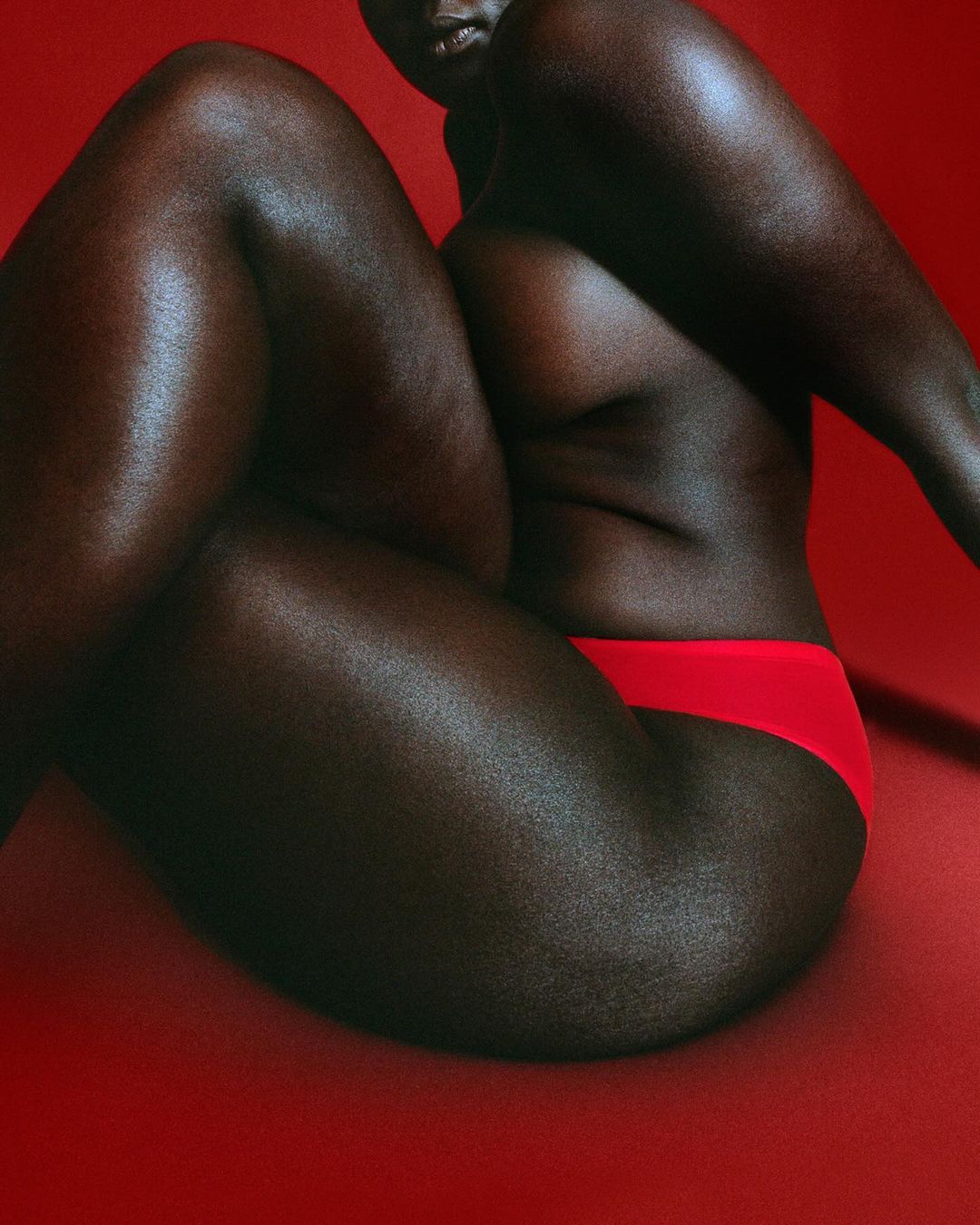Close-up studio shot of a Black woman in red underwear, showcasing her body against a red background with soft, diffused lighting.