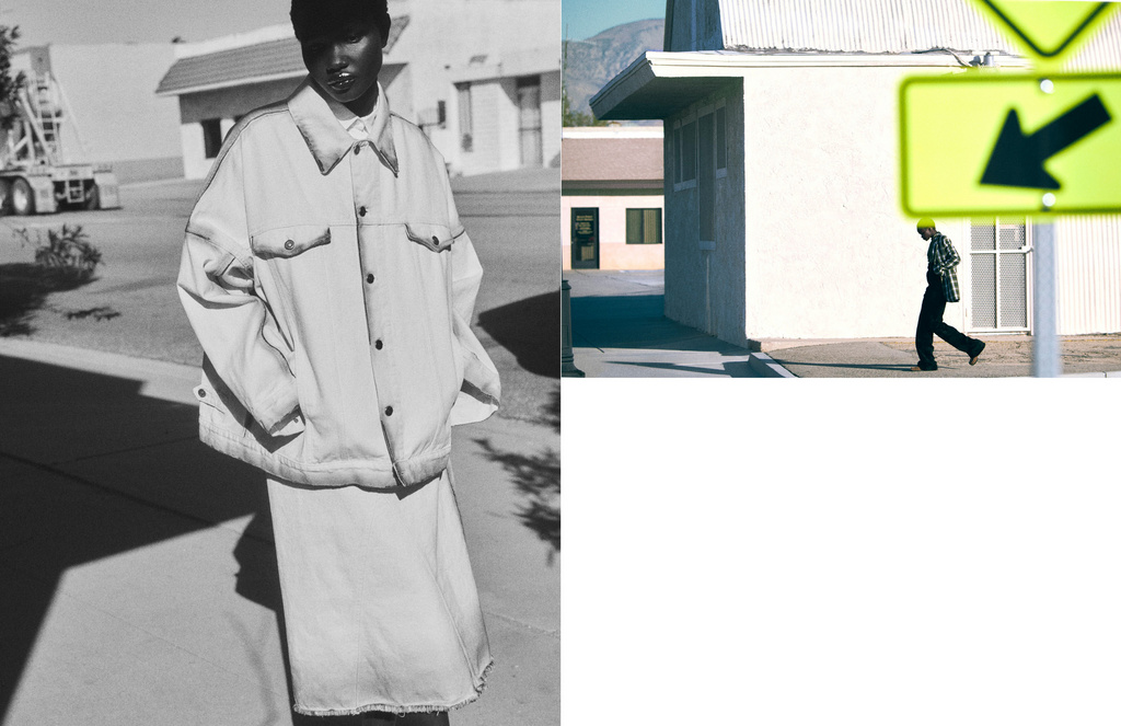 Fashion shot: a Black model poses in an oversized white denim jacket and skirt on a monochrome outdoor street next to a passing pedestrian.