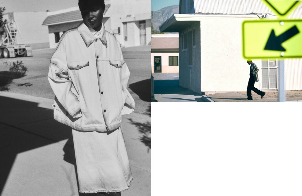 Fashion shot: a Black model poses in an oversized white denim jacket and skirt on a monochrome outdoor street next to a passing pedestrian.