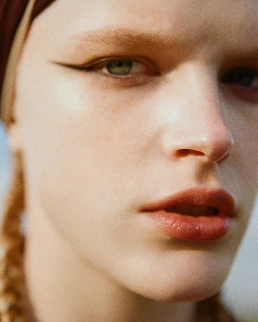 Close-up portrait of a young woman with fair skin and green eyes, wearing a headscarf and eyeliner, shot in natural lighting.