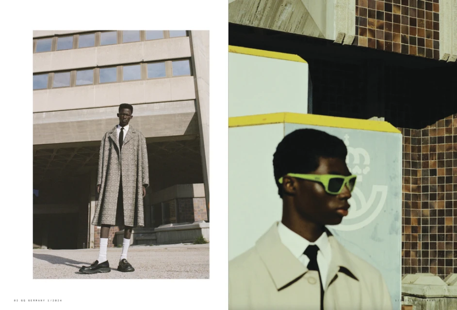 Fashion shot of two Black men in trench coats and suits, one wearing green sunglasses, in an urban setting with brutalist architecture.