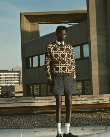 Black man standing on a rooftop wearing a patterned brown sweater and dark shorts photographed by Julia Noni.