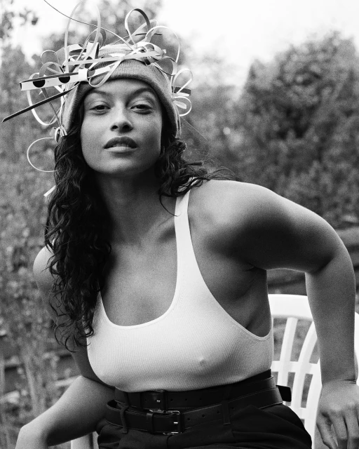Black and white portrait of a woman wearing a beanie and tank top, accessorized with a decorative headpiece, posing outdoors.