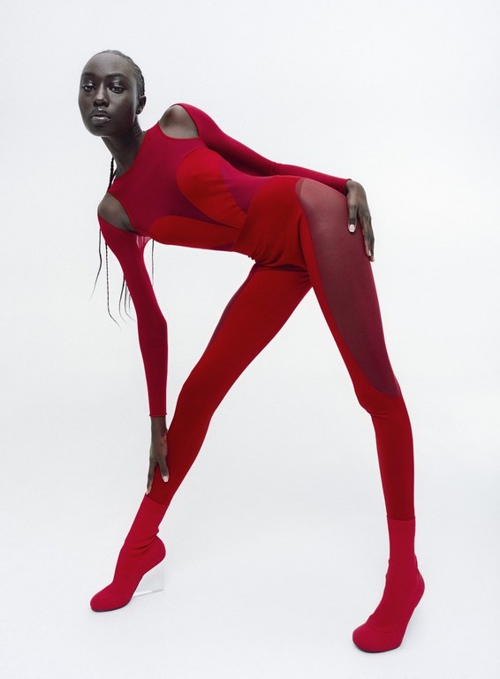 Fashion shot of a Black female model in a red bodysuit bending over in a studio. The image features modern design and a minimalist aesthetic.