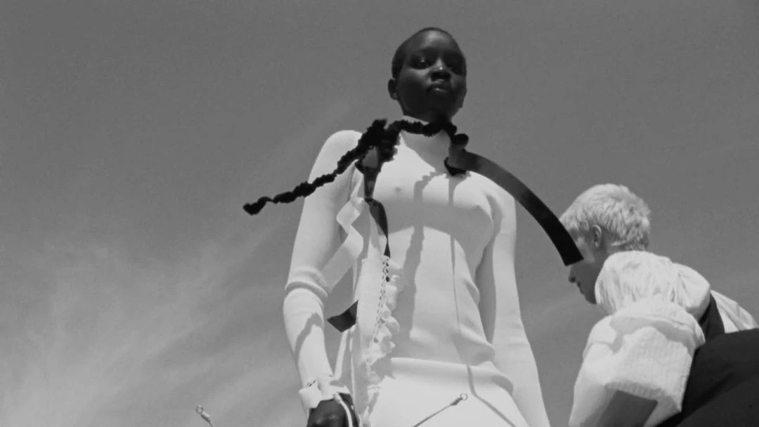Black and white fashion shot of an African-descent adult female in a white dress with ribbon and a white adult female in the background.