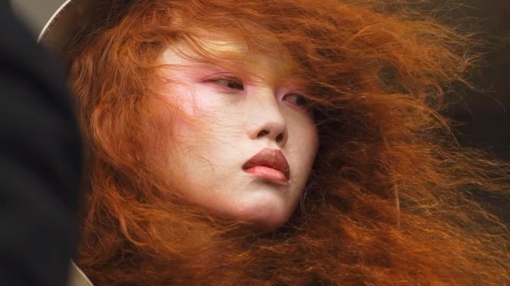 Close-up of an adult female with pink eye makeup and red hair styled into a voluminous, flowing look. Fashion and beauty concept.