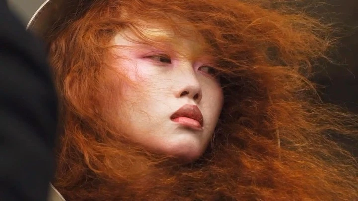 Close-up of an adult female with pink eye makeup and red hair styled into a voluminous, flowing look. Fashion and beauty concept.