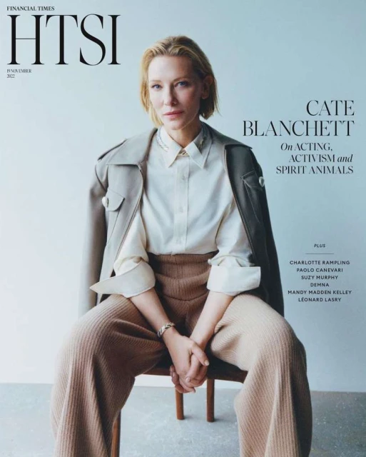 Cate Blanchett sits for a magazine cover, showcasing a beige trench coat, light shirt, and tan trousers against a neutral backdrop.