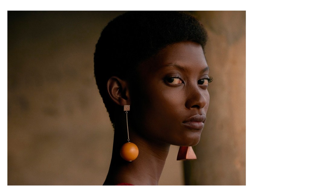 Close-up portrait of a Black female model with stylish brown earrings against a blurred warm-toned background, creating a striking beauty shot.