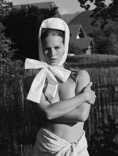 Black-and-white portrait of a woman with a towel wrapped around her waist and a white headscarf with a bow, outdoors.
