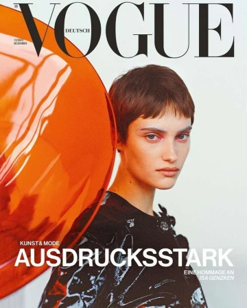 Vogue Deutsch magazine cover featuring a model with short brown hair, posing in a shiny black top and orange translucent material.