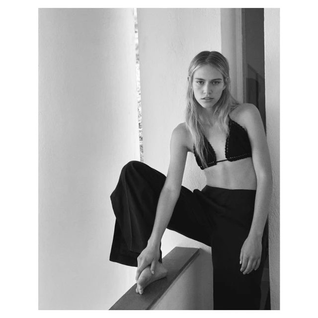Monochrome portrait of a woman wearing a bra top and palazzo pants, posing indoors with natural light and a minimalist aesthetic.