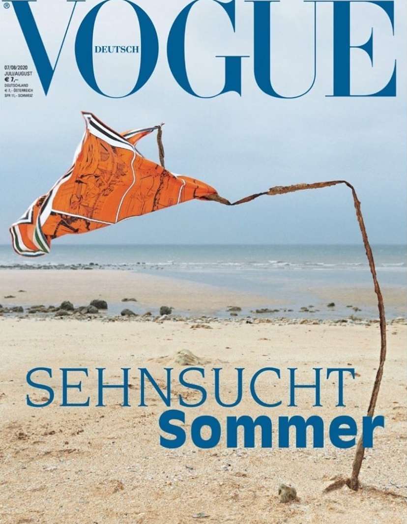 Vogue Deutsch cover featuring a large orange kite, sand, and a beach on a cloudy day. The image evokes the feeling of summer.