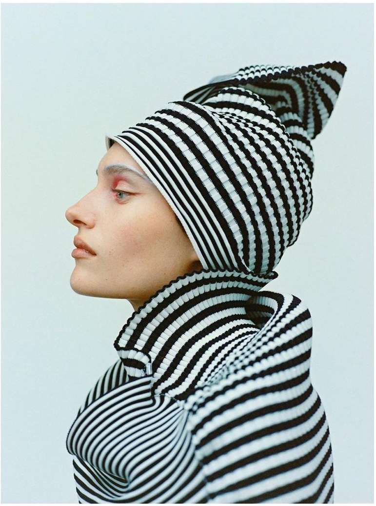 Profile shot of a model wearing a black and white striped hat and top against a plain light blue background, studio lighting.