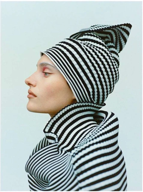 Profile shot of a model wearing a black and white striped hat and top against a plain light blue background, studio lighting.