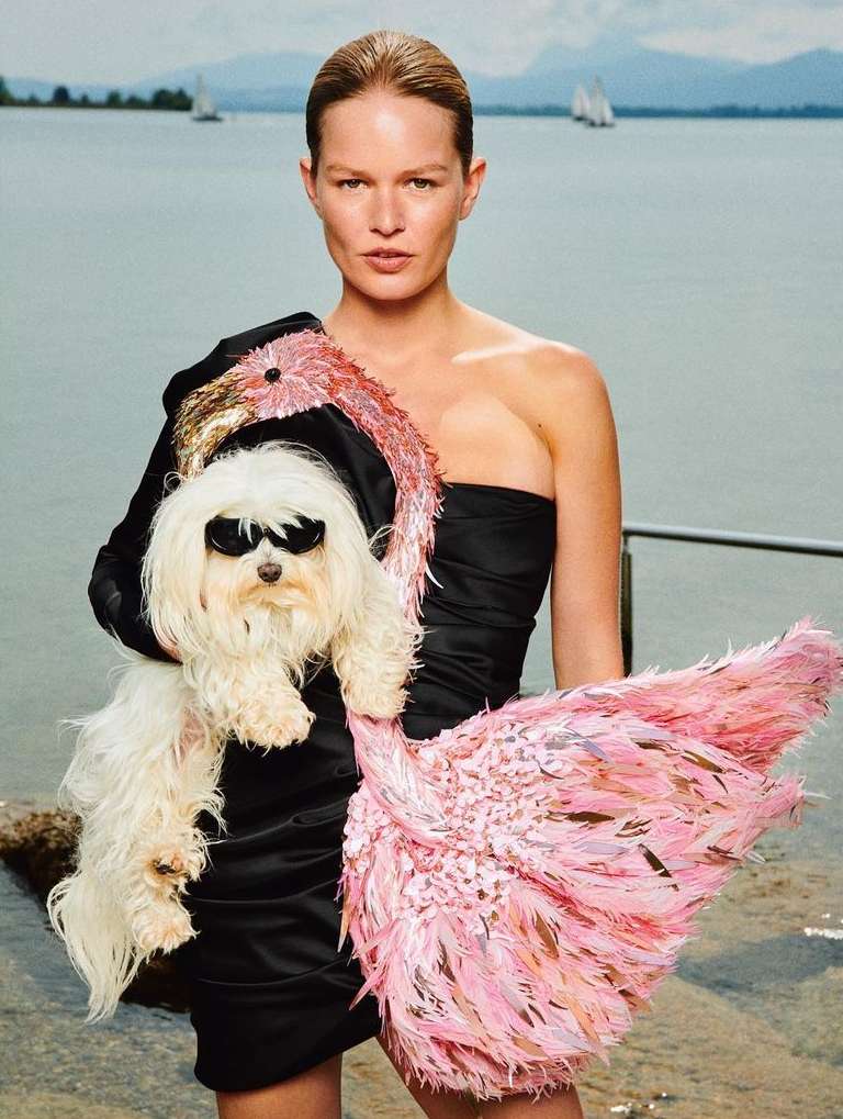 Woman in black dress holds white dog wearing sunglasses on lakeside with sailboats in background, fashion, beauty, and lifestyle.