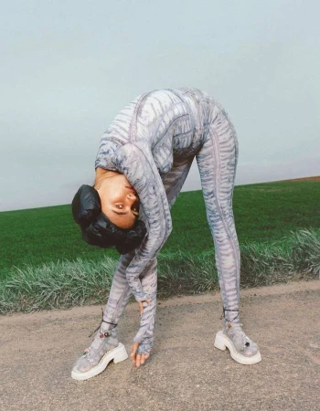 Model wearing a printed bodysuit and platform shoes bending backward on an outdoor road by photographer Julia Noni.