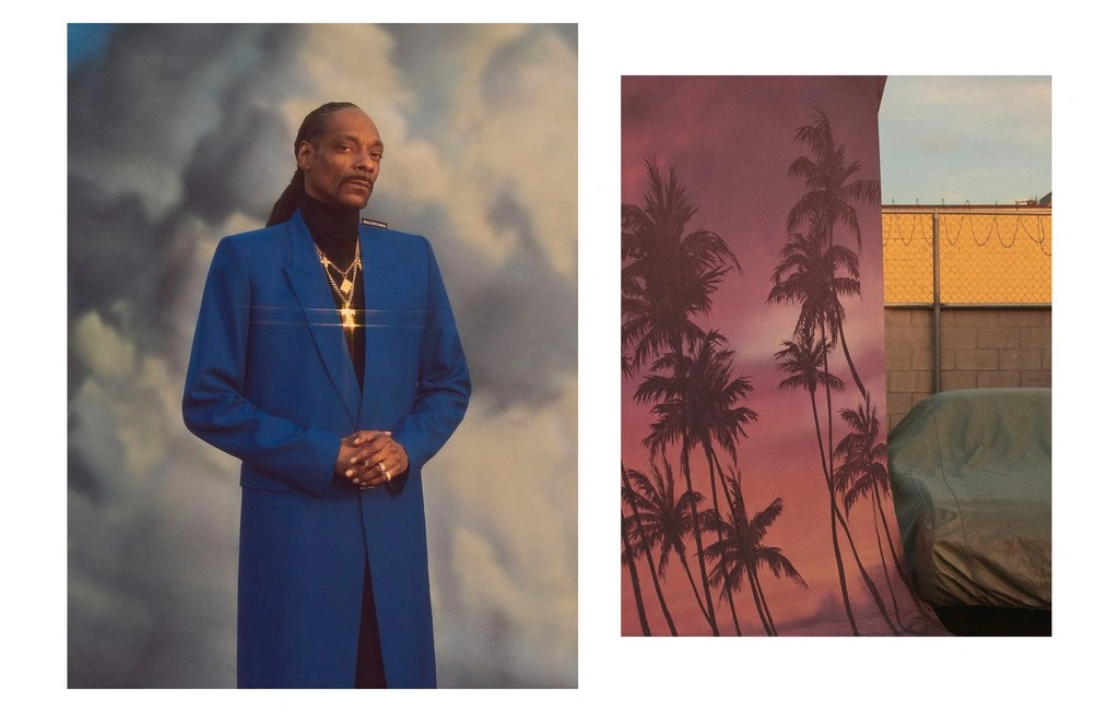 Snoop Dogg wearing a blue coat and turtleneck against a cloudy sky backdrop, beside a palm tree backdrop photo