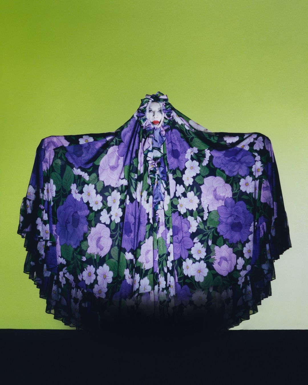 Artistic portrait of a person covered in a floral fabric, with a green background. Fashion and creative expression combine in this surreal image.