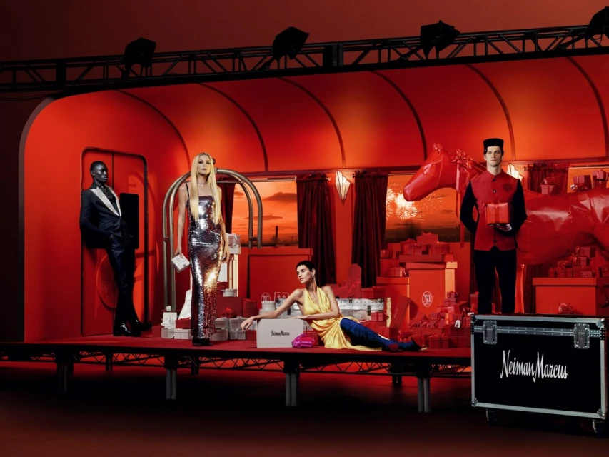 Stylized fashion set featuring models in evening wear in a faux train car setting with gift boxes and a vintage aesthetic.