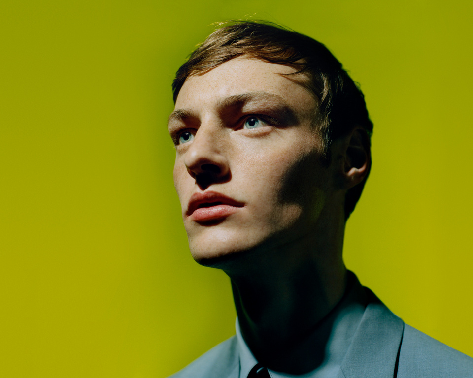 Portrait of a man in a blue shirt with a solid yellow background by photographer Scandebergs