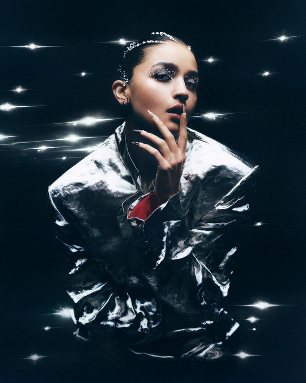 Glamorous portrait of a young adult female model with glitter makeup wearing a shiny silver jacket and posing in a dark studio.