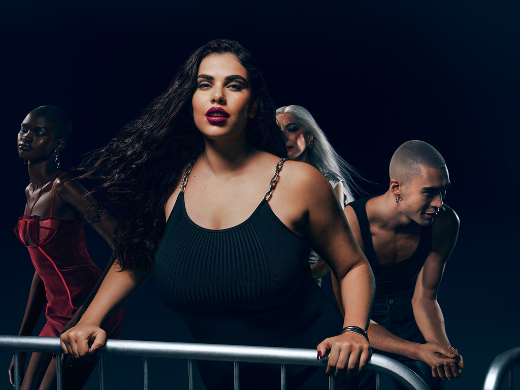 Diverse group of four fashion models in a dimly lit studio, showcasing makeup, hairstyles, and clothing against a dark background.