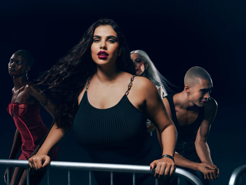 Diverse group of four fashion models in a dimly lit studio, showcasing makeup, hairstyles, and clothing against a dark background.