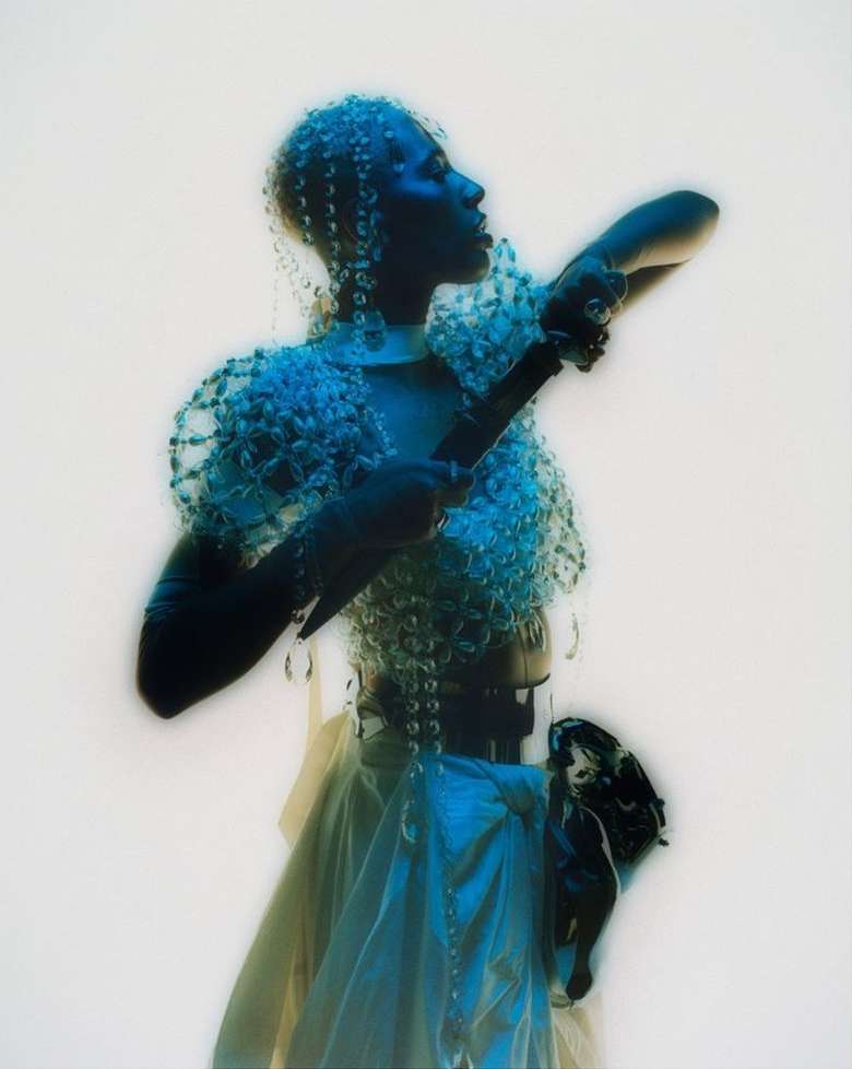 Woman poses in an ornate beaded outfit, captured in a medium shot with white backdrop, showcasing fashion and design elements.