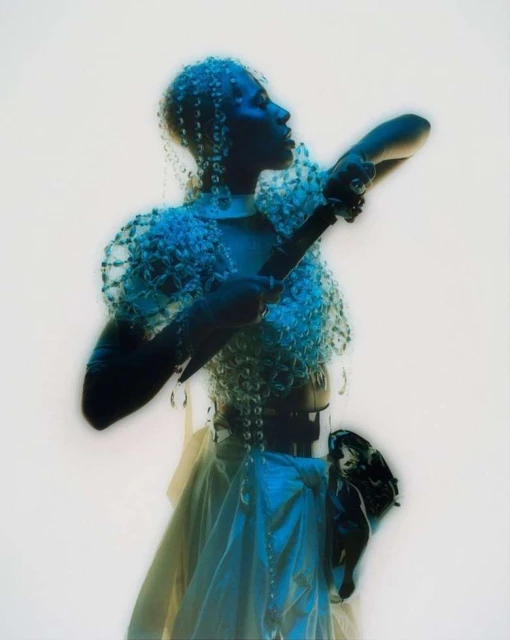 Woman poses in an ornate beaded outfit, captured in a medium shot with white backdrop, showcasing fashion and design elements.